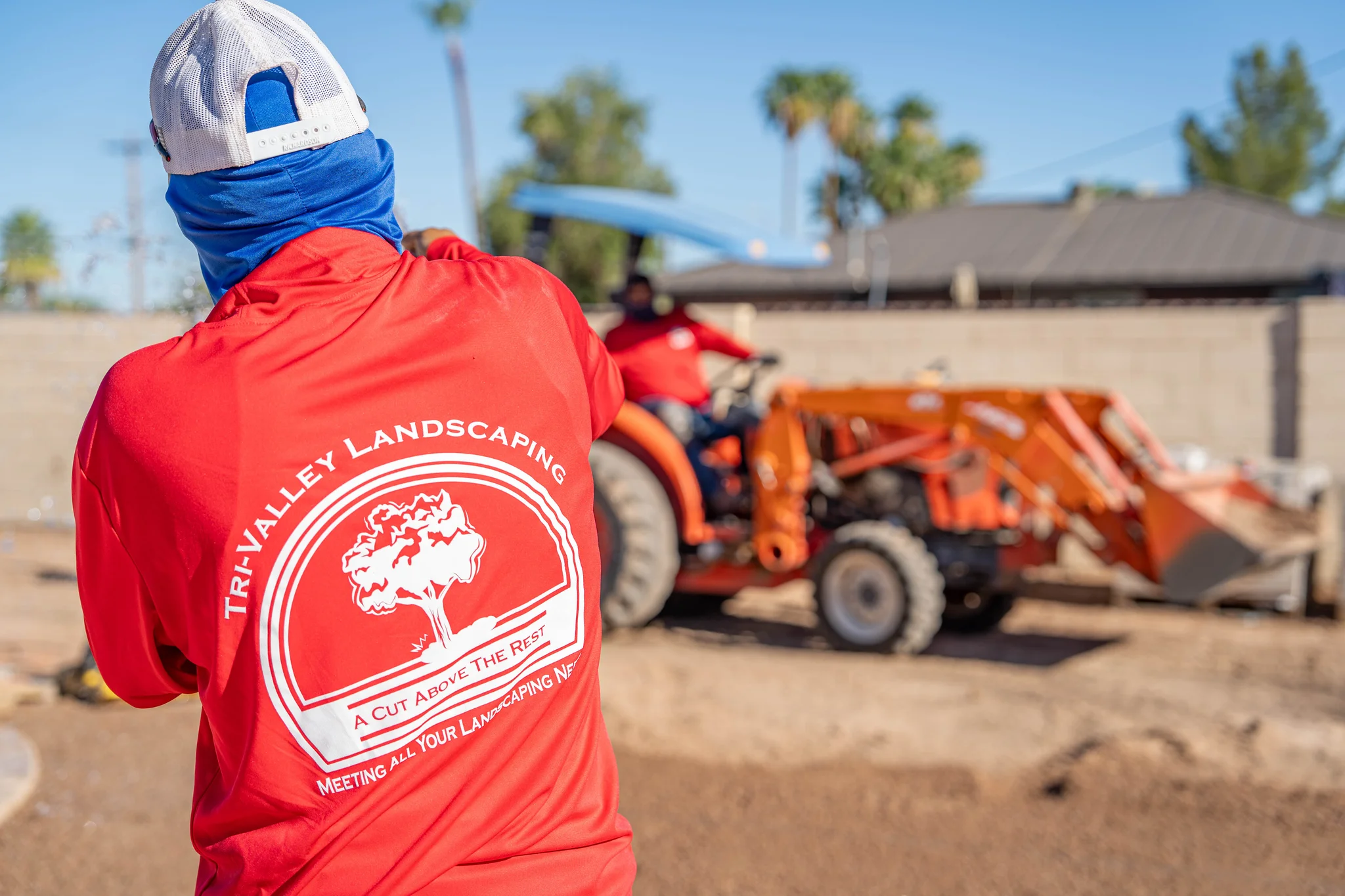 Landscaping workers operate orange tractor at sunny job site
