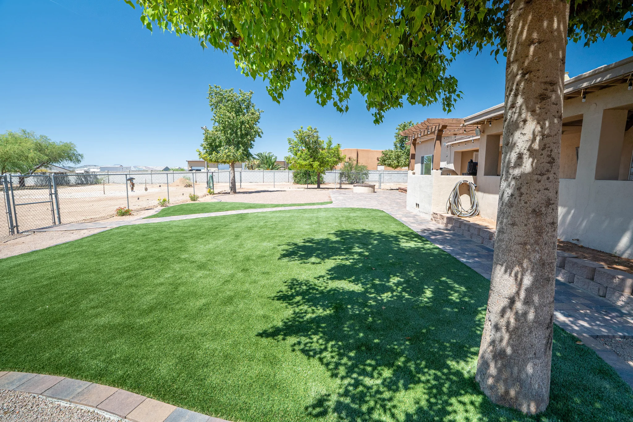 Shaded backyard with artificial turf, trees, and patio