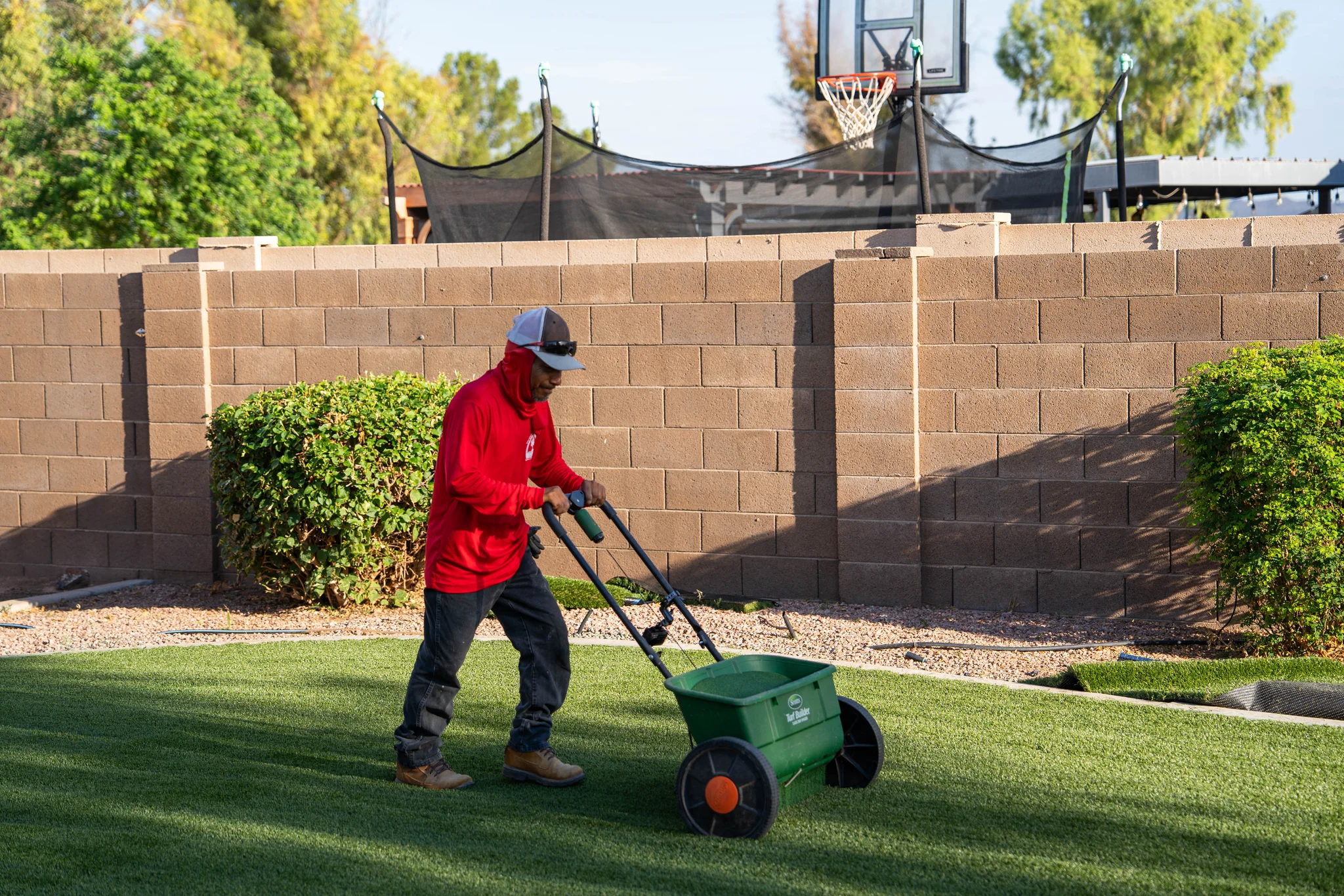 Landscaper spreads material across artificial turf in backyard