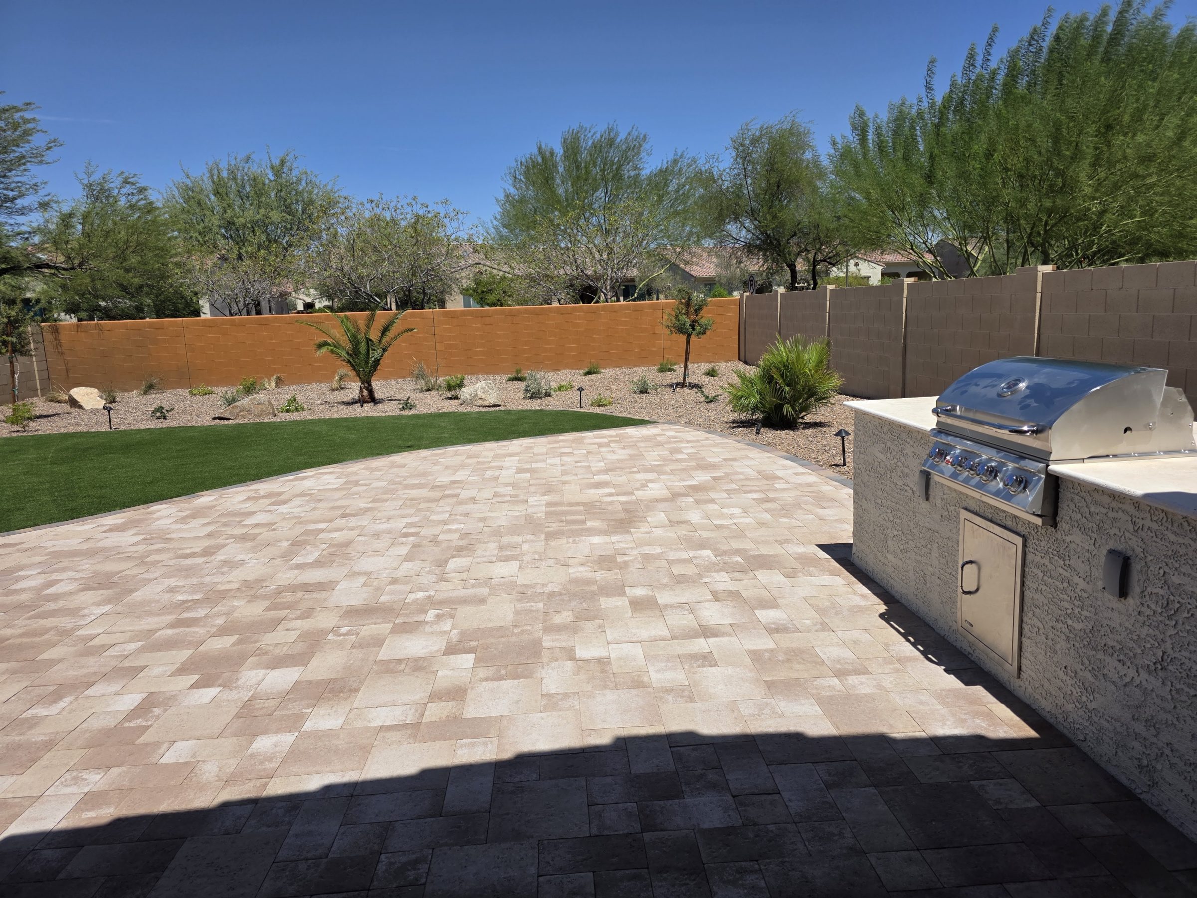 Sunlit tiled backyard patio with outdoor grill and desert landscaping