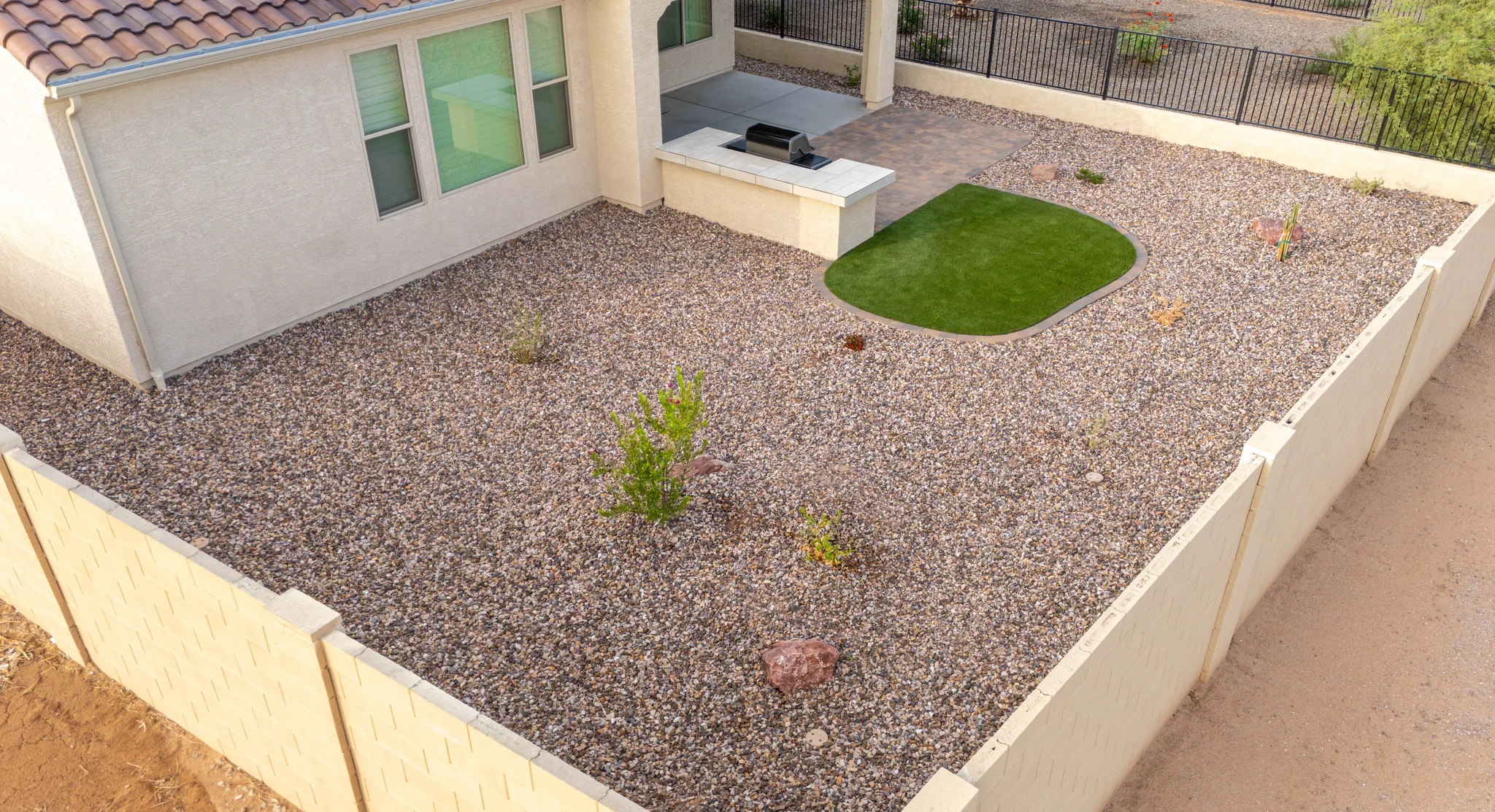 Gravel backyard with artificial turf, grill, and patio
