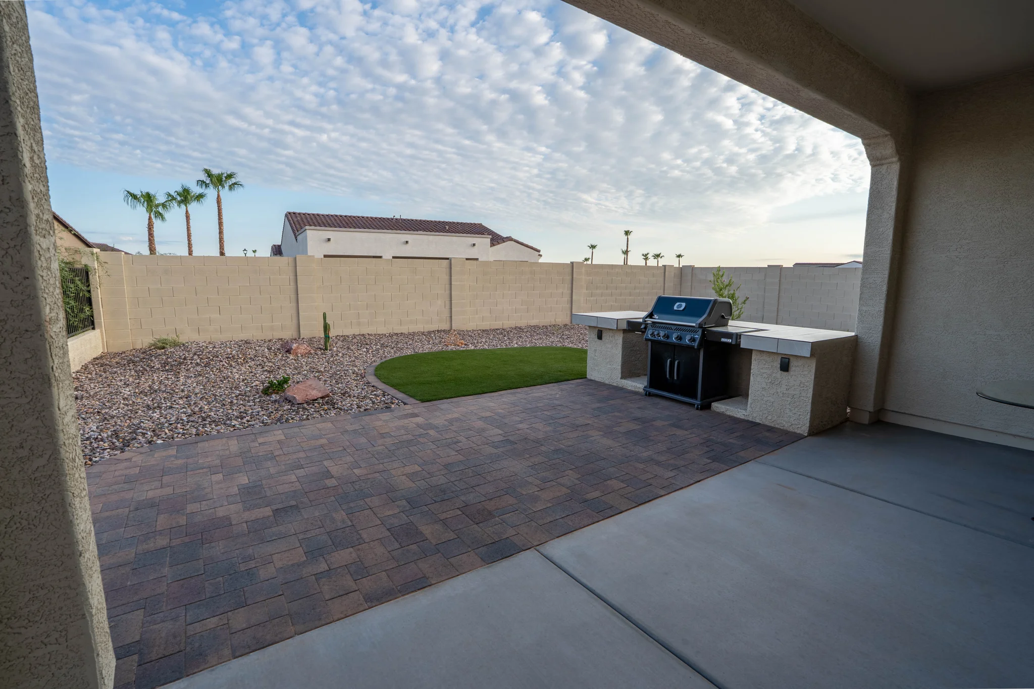 Covered patio with grill, pavers, turf, and palm trees