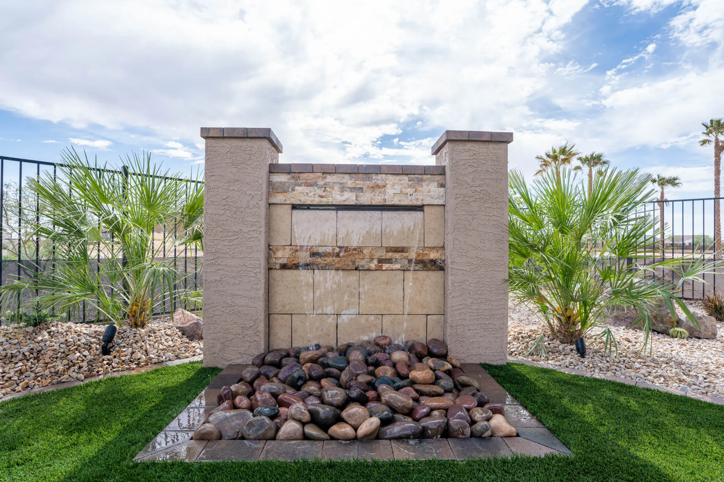 Stone water feature surrounded by palms and lawn