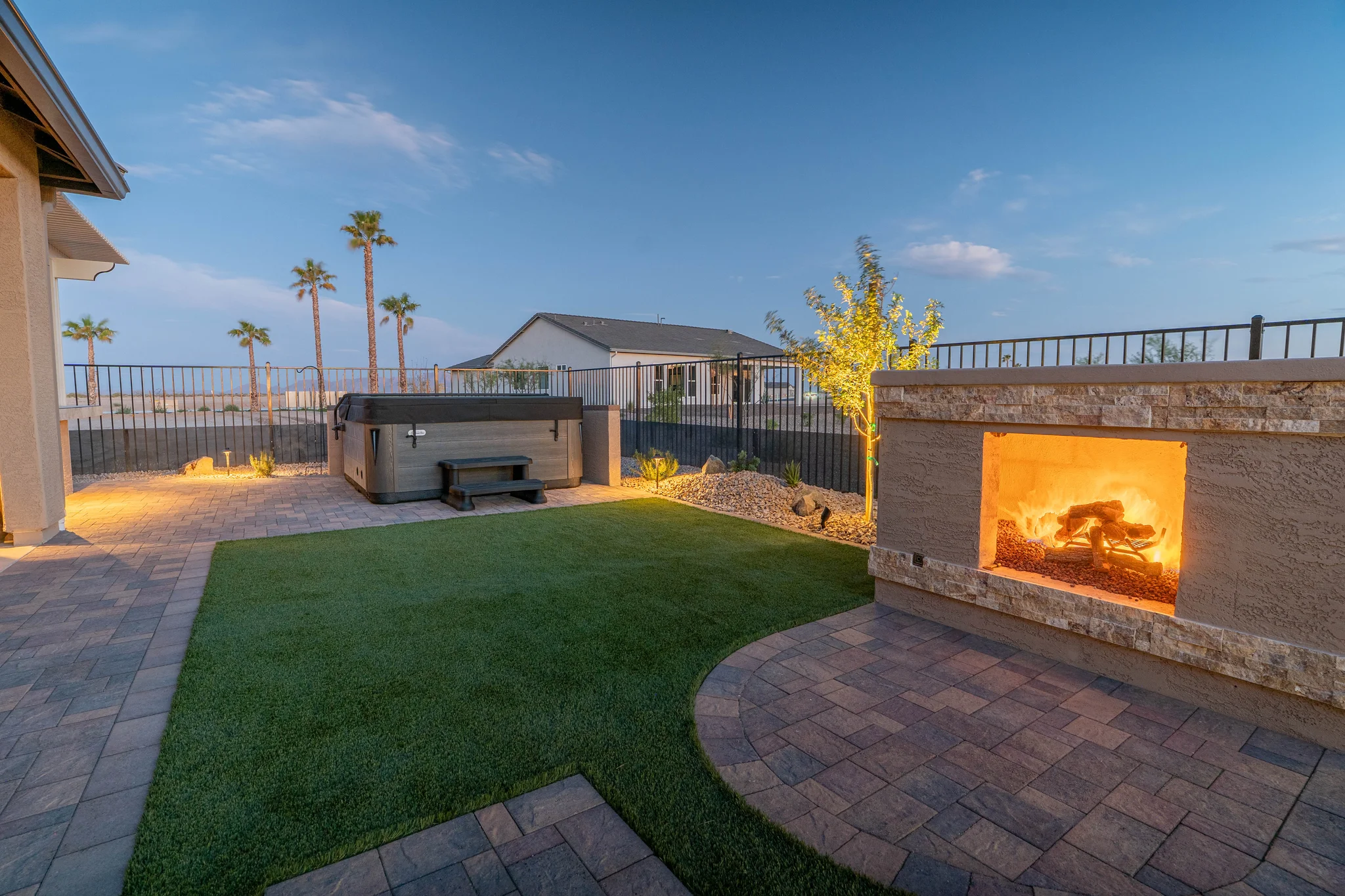 Twilight patio with fire pit, hot tub, and palm trees