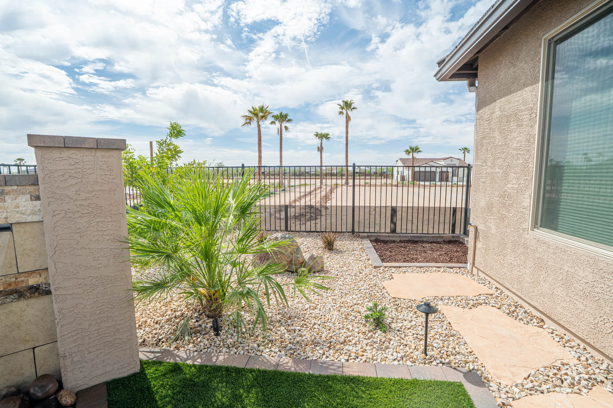 Desert-style backyard with palms, gravel landscaping, and black fence