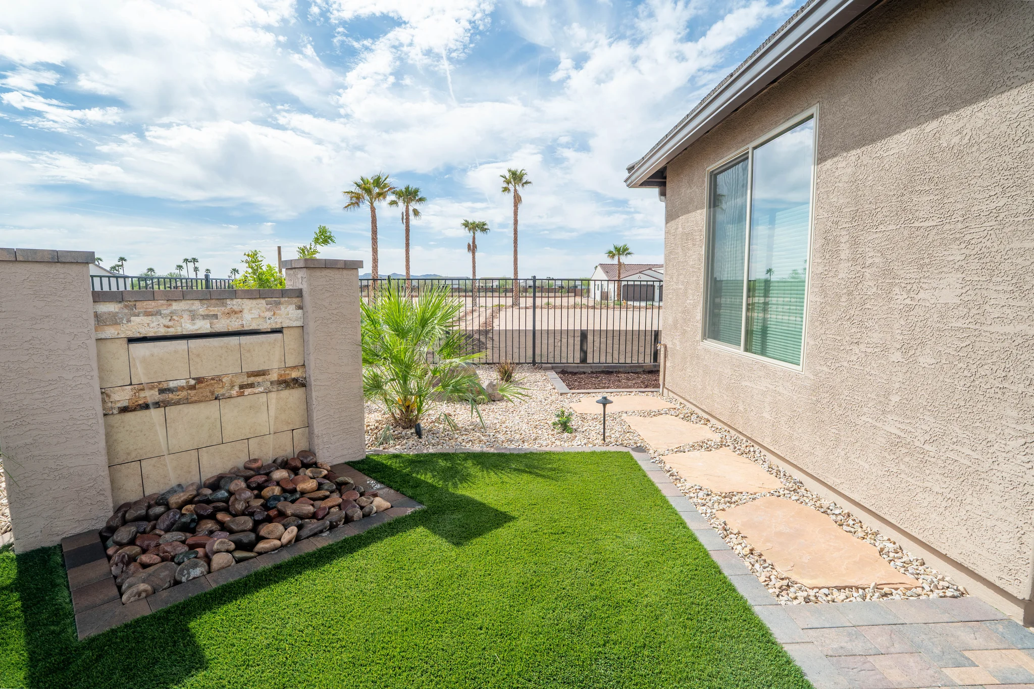 Desert backyard with turf, stone path, palms, and fence