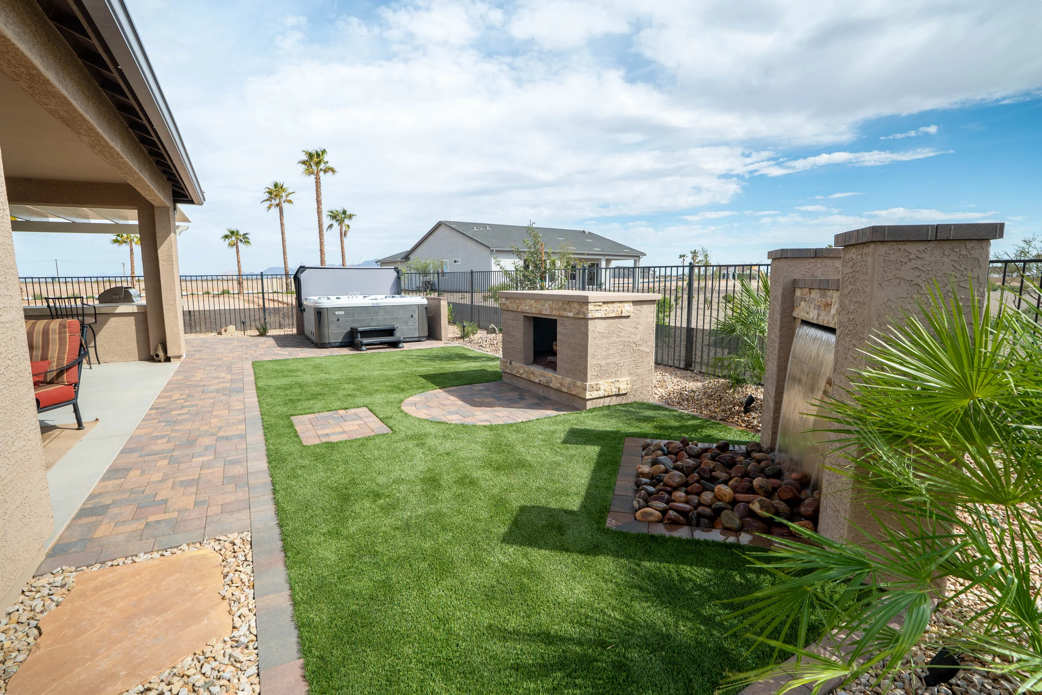 Landscaped backyard with fireplace, waterfall, and hot tub