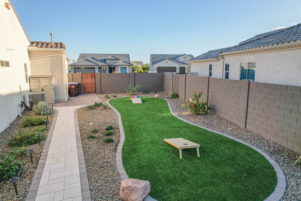 Landscaped backyard with artificial turf and cornhole boards