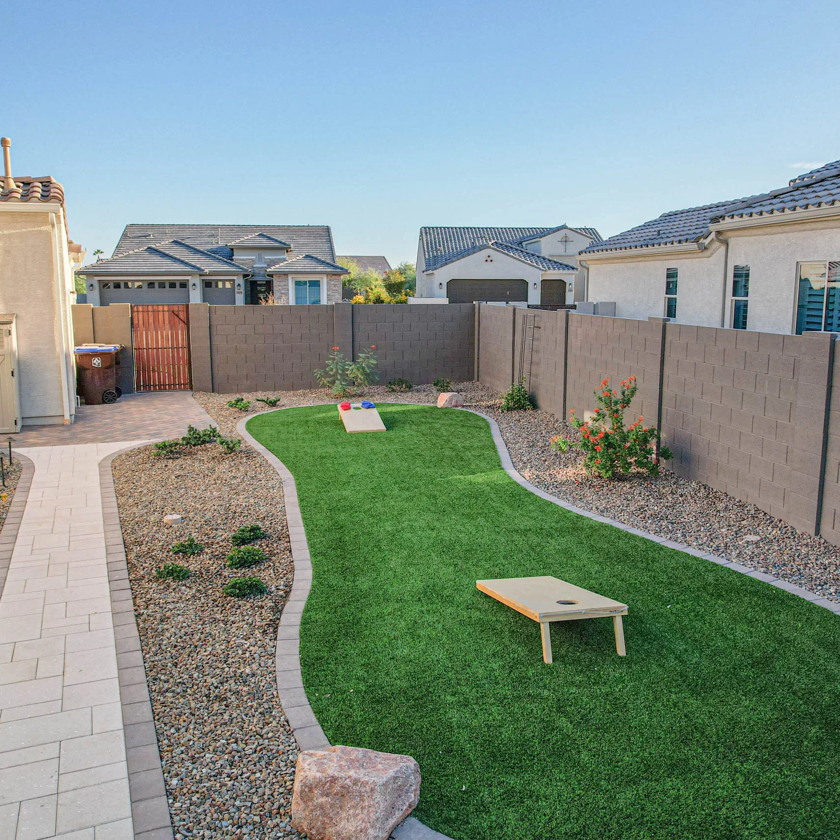 Landscaped backyard with artificial turf and cornhole boards