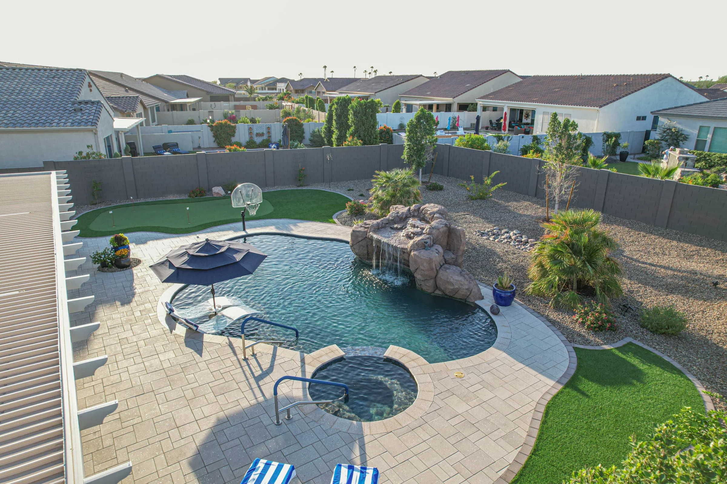 Landscaped backyard pool with waterfall, putting green, and basketball hoop