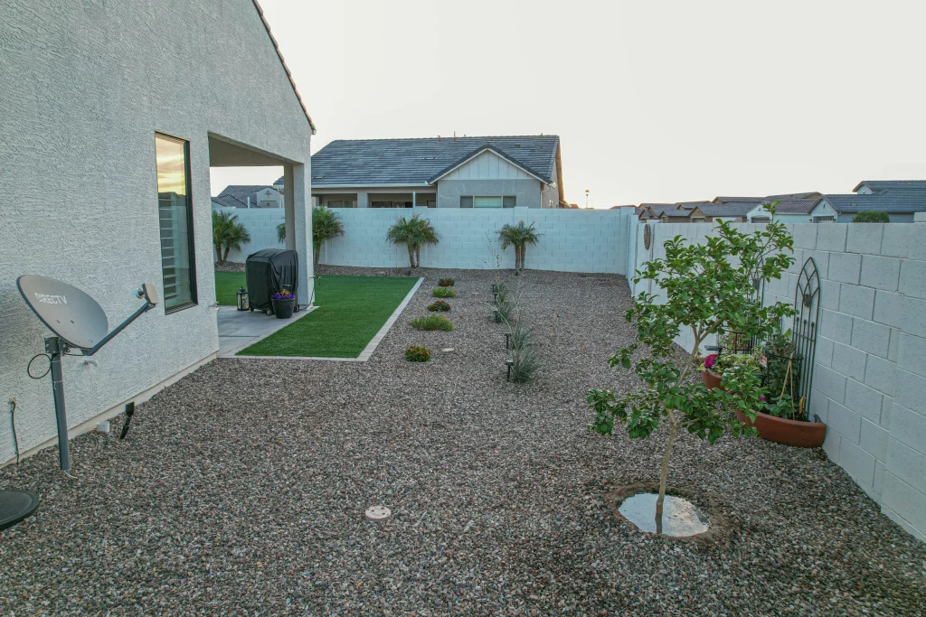 Gravel backyard with garden beds, palms, and artificial turf