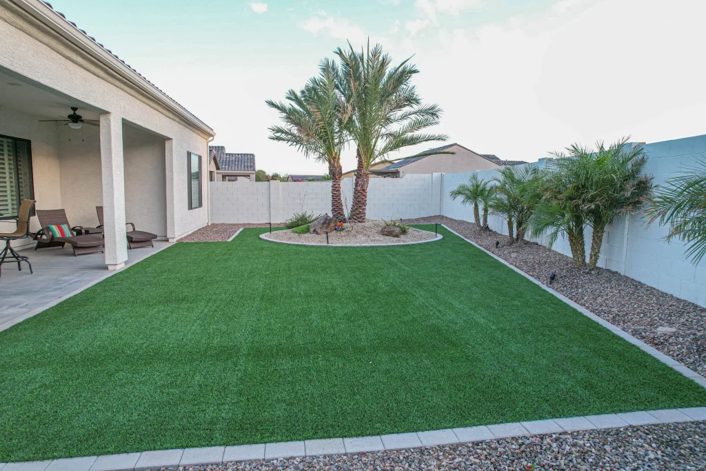 Landscaped backyard with artificial turf, palms, and covered patio