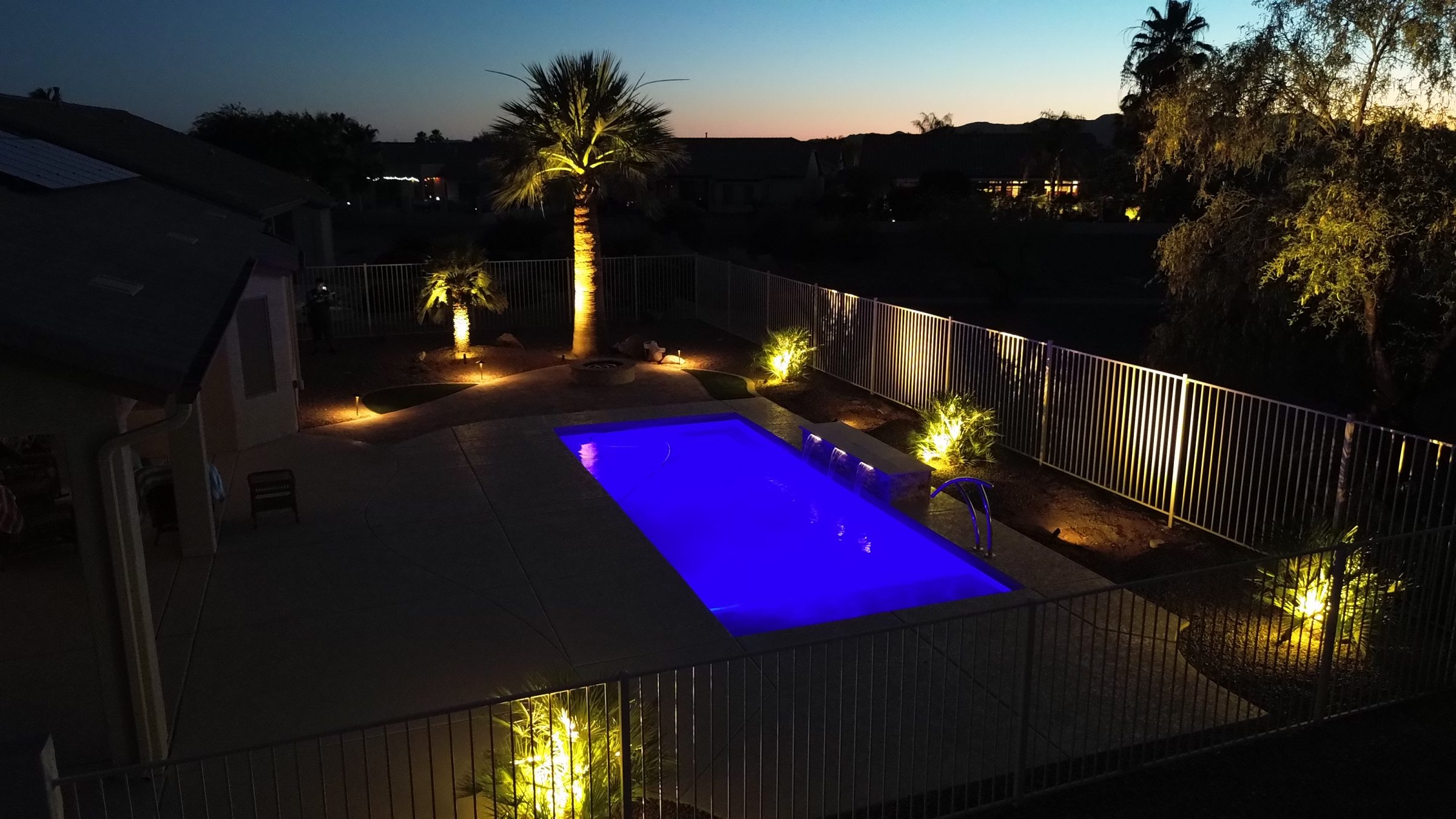 Blue-lit backyard pool with illuminated palm trees at dusk