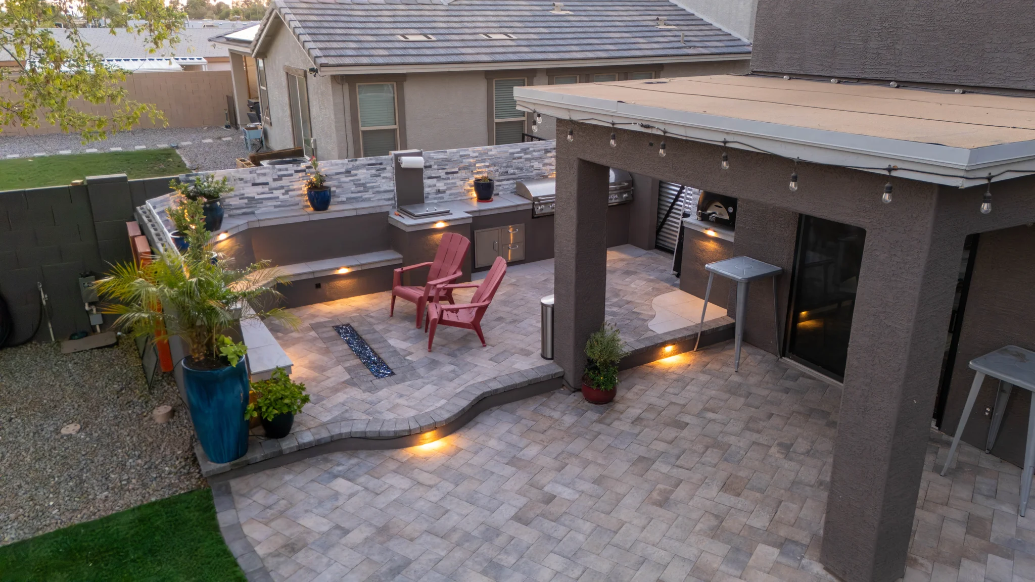 Twilight backyard patio with outdoor kitchen and red chairs