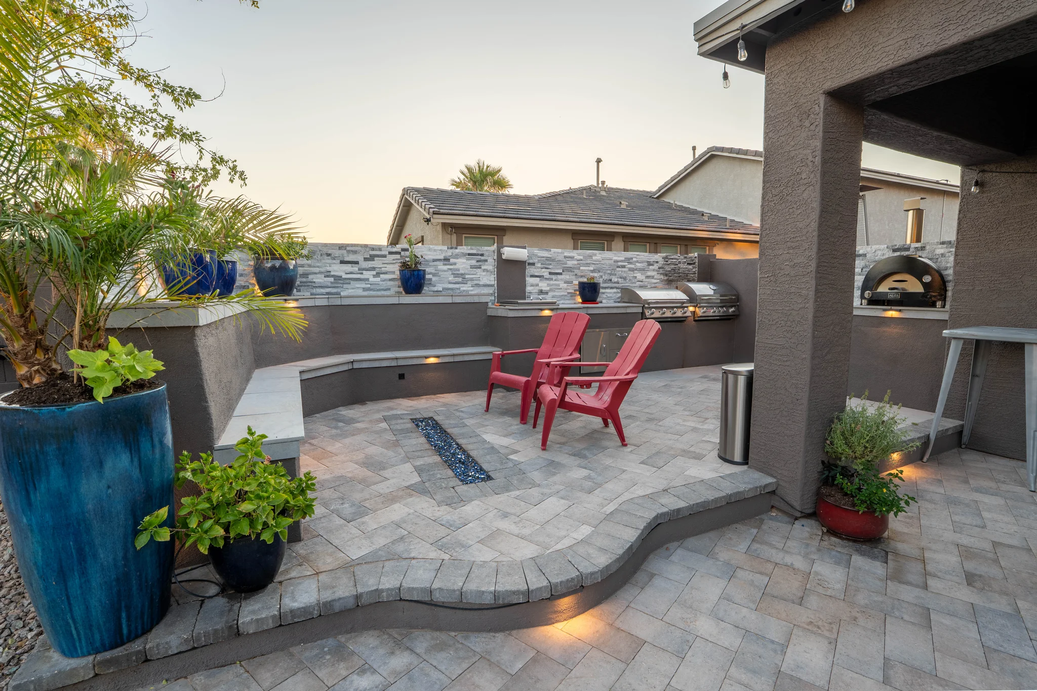 Modern backyard kitchen patio with red chairs and blue planters