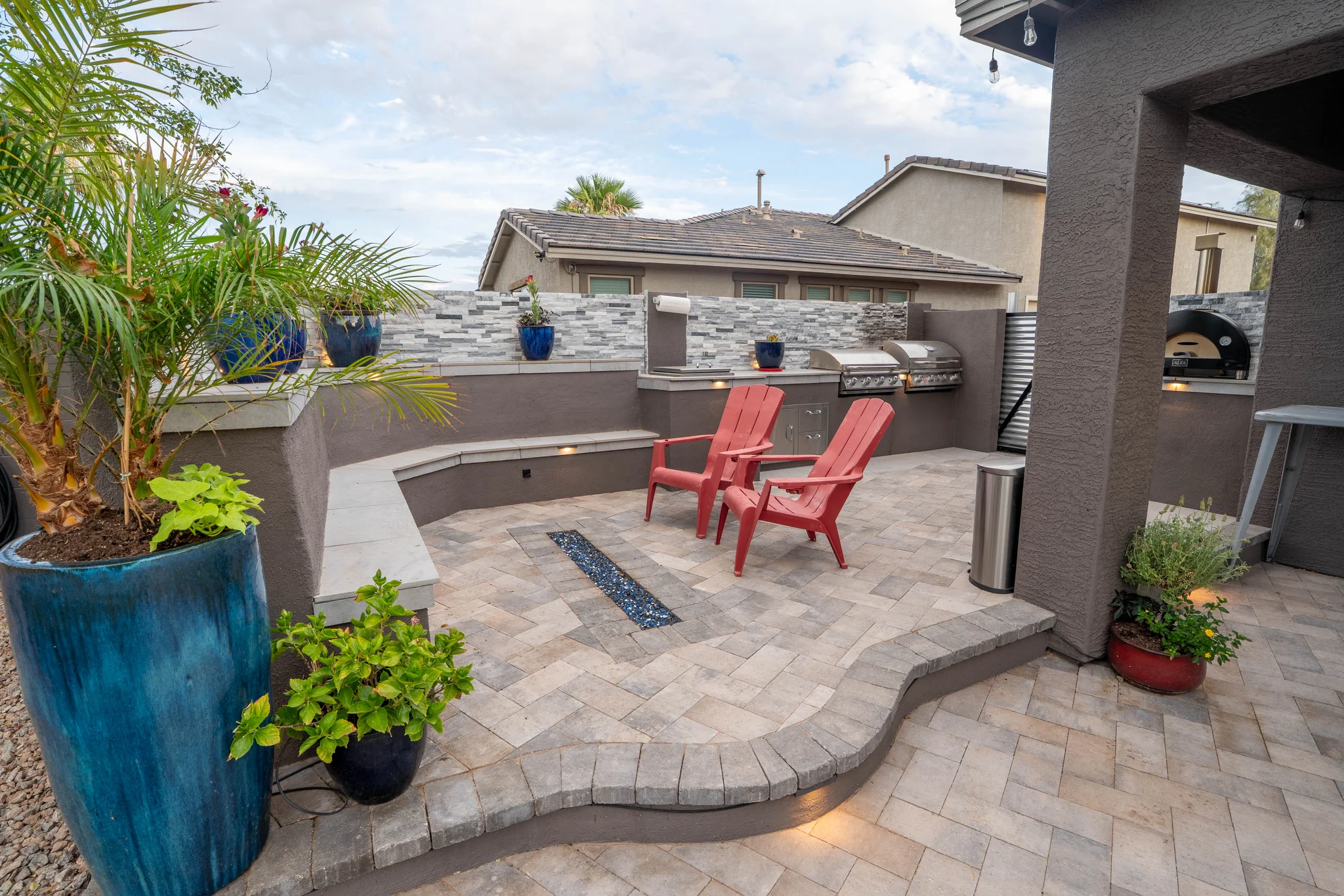 Paved backyard patio with red chairs and outdoor kitchen