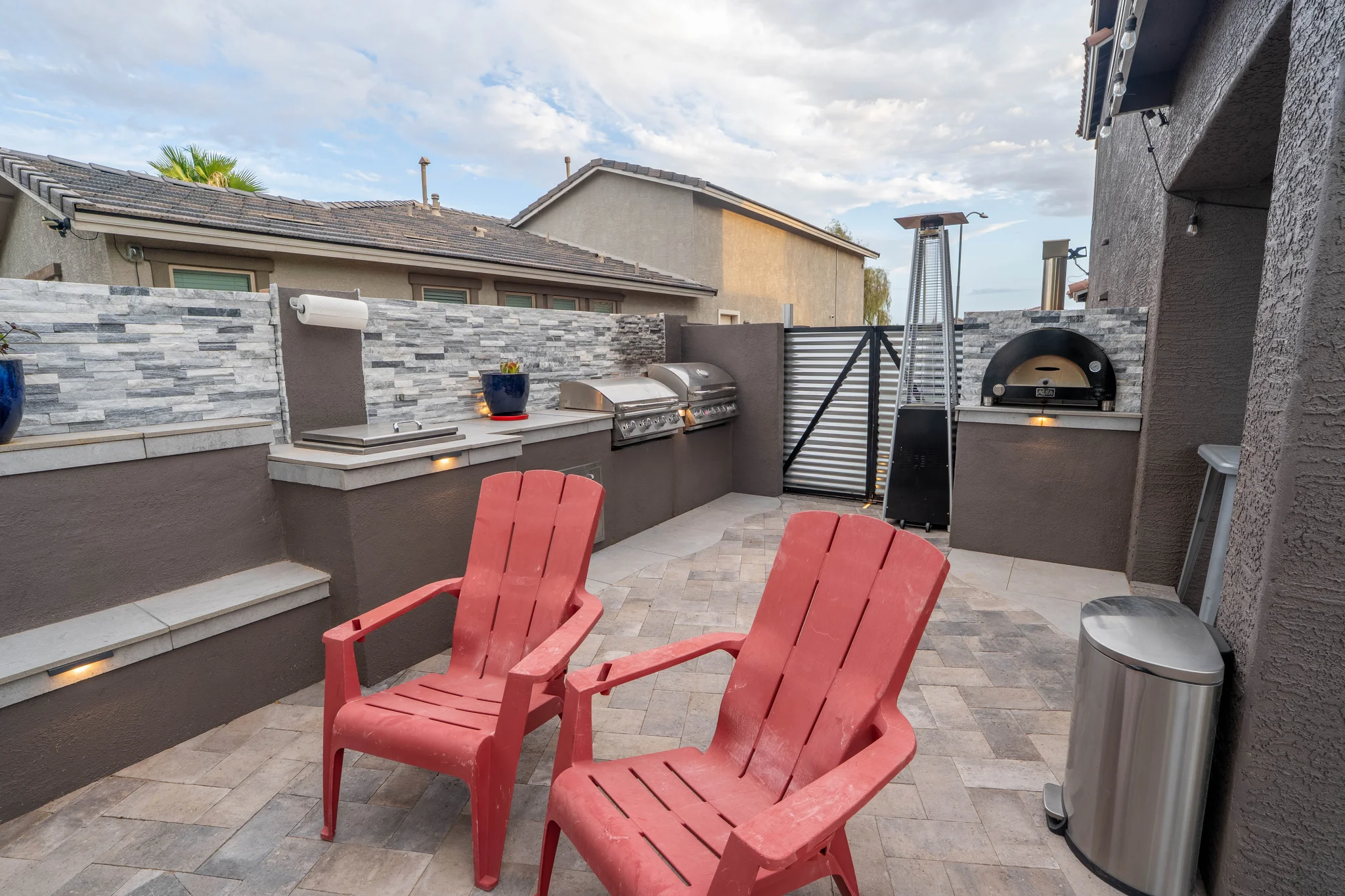Outdoor kitchen patio with grills, pizza oven, and red chairs