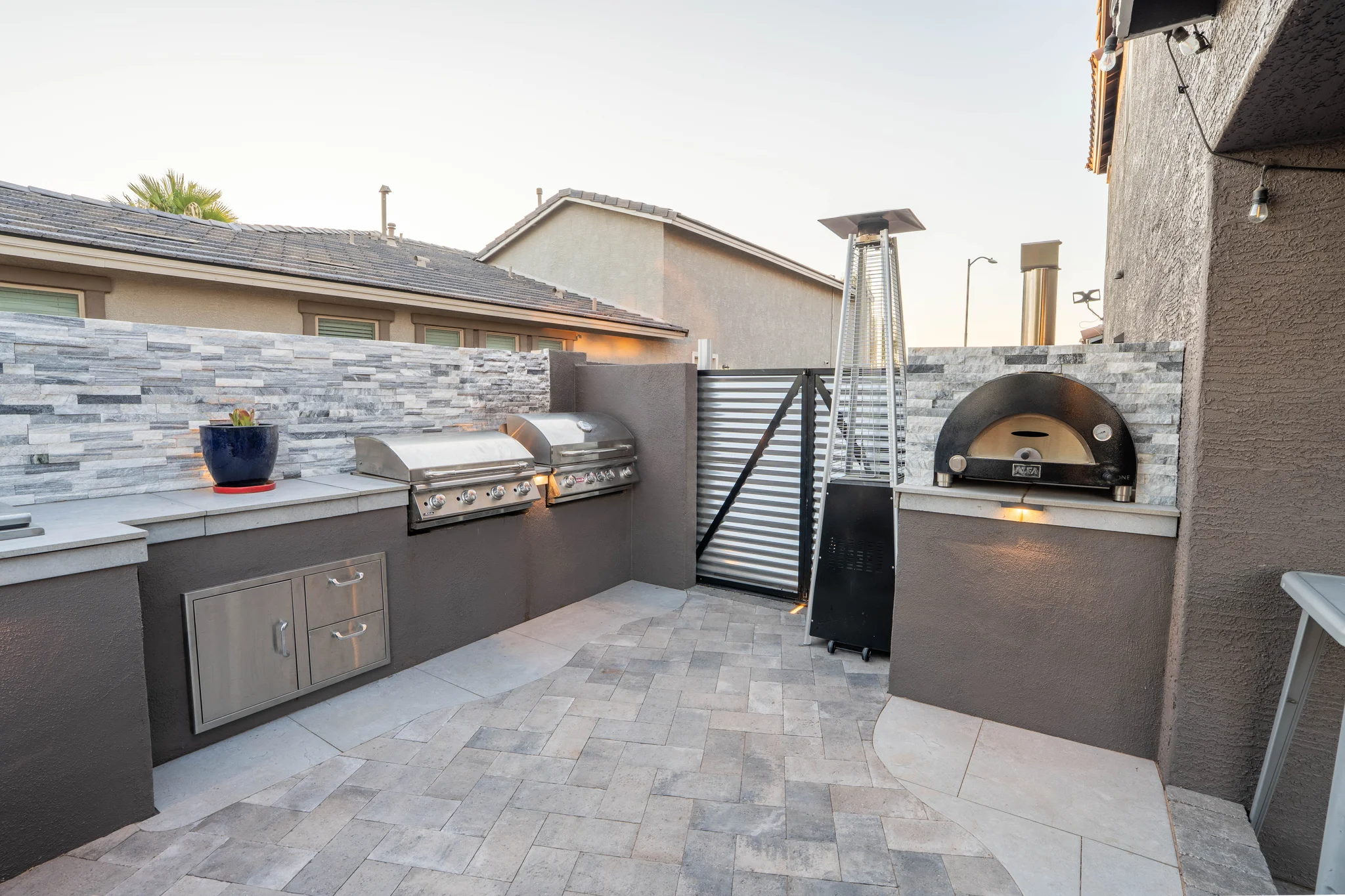 Modern outdoor kitchen with grills, pizza oven, and patio heater