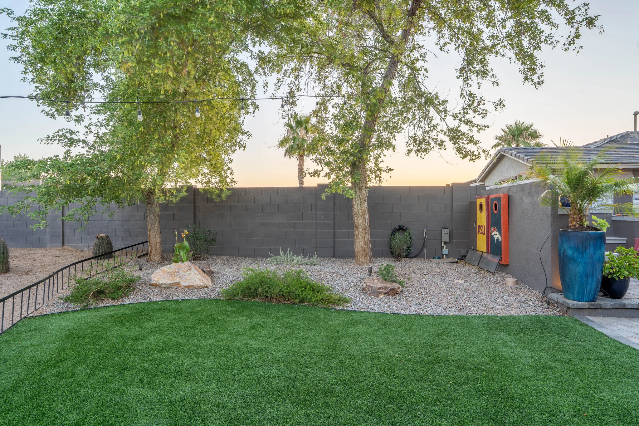 Landscaped backyard with artificial turf, trees, and string lights