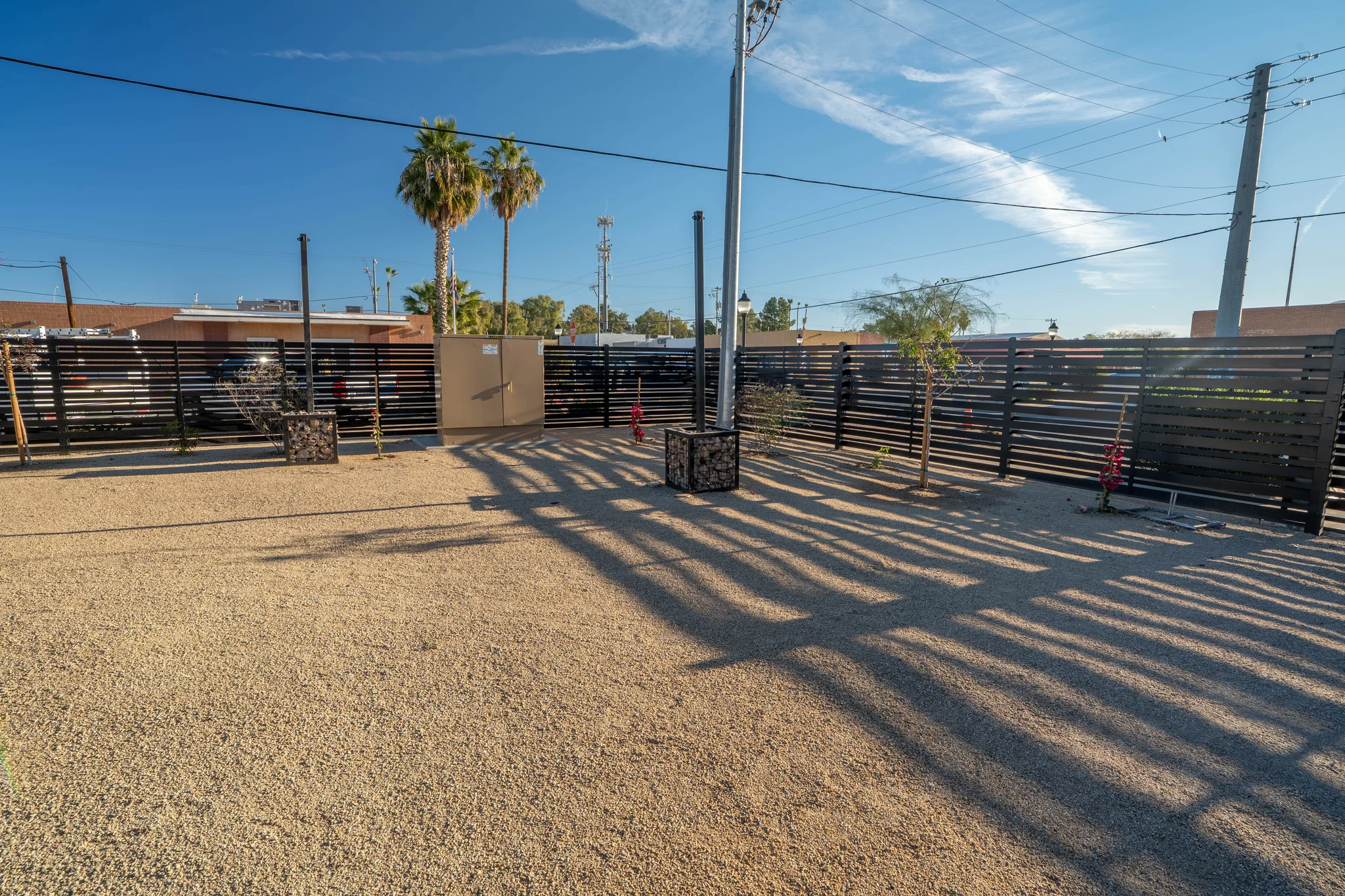 Gravel yard with black fence, utility poles, and palms