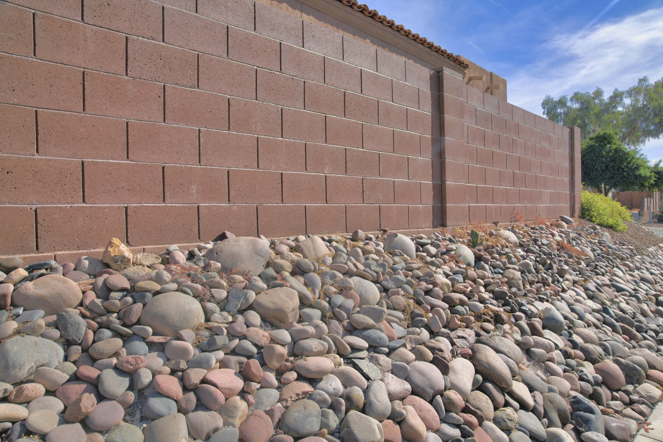 Brown block wall beside a landscaped bed of river rocks