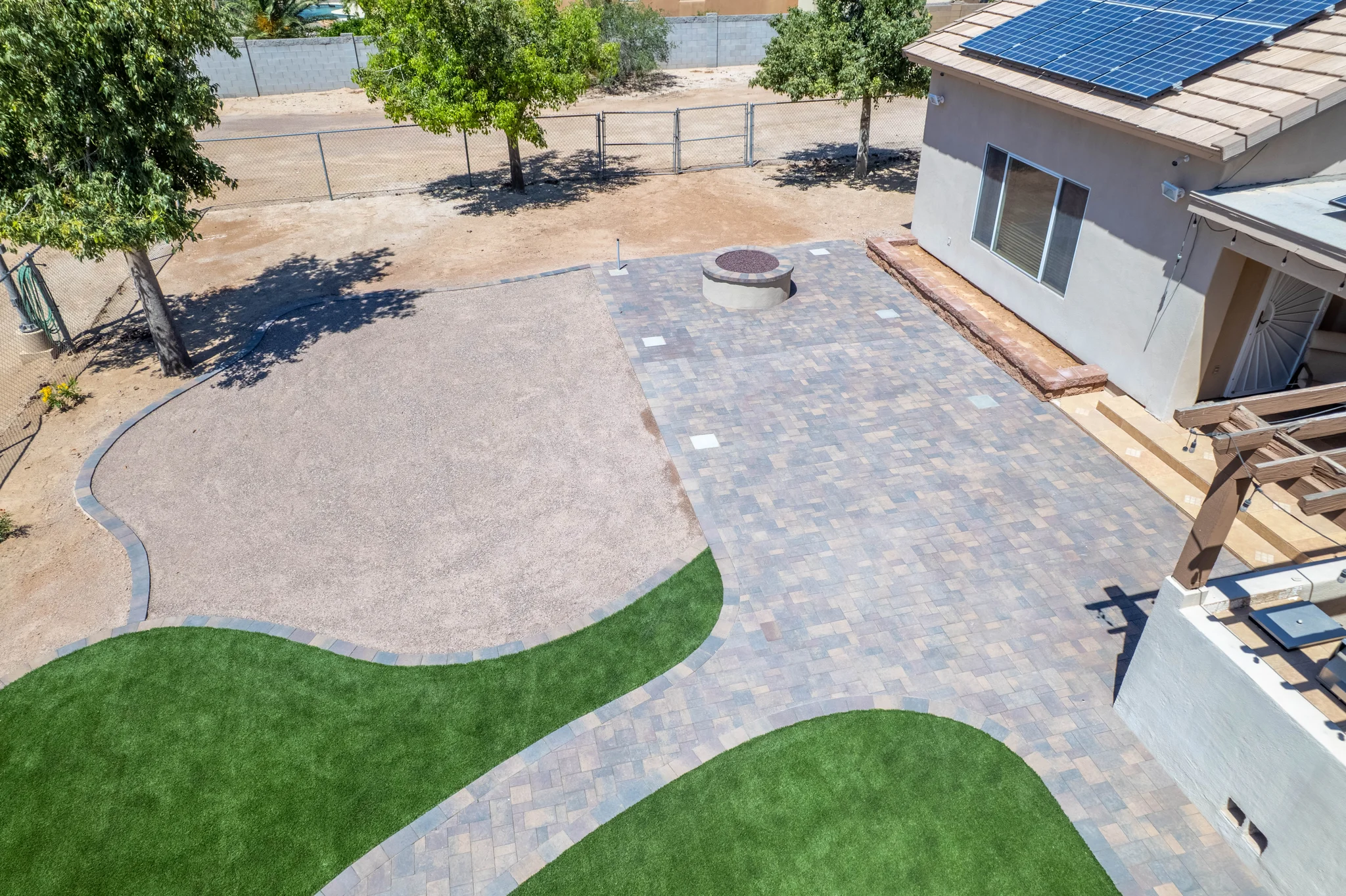 Paved backyard patio with fire pit and artificial turf