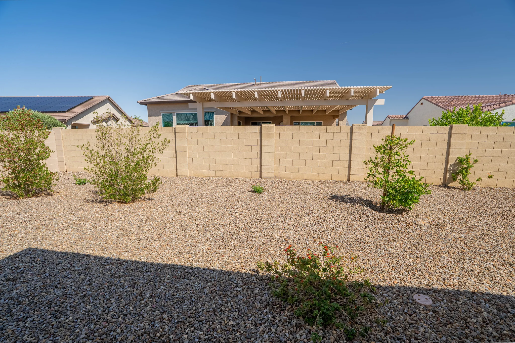 Gravel backyard with shrubs, block wall, and pergola