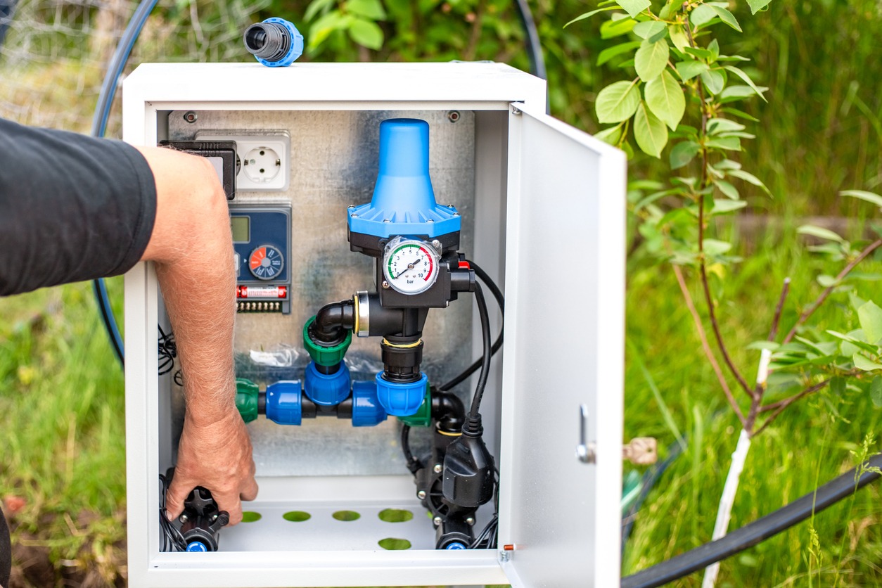 Technician adjusts outdoor irrigation control box with pressure gauge