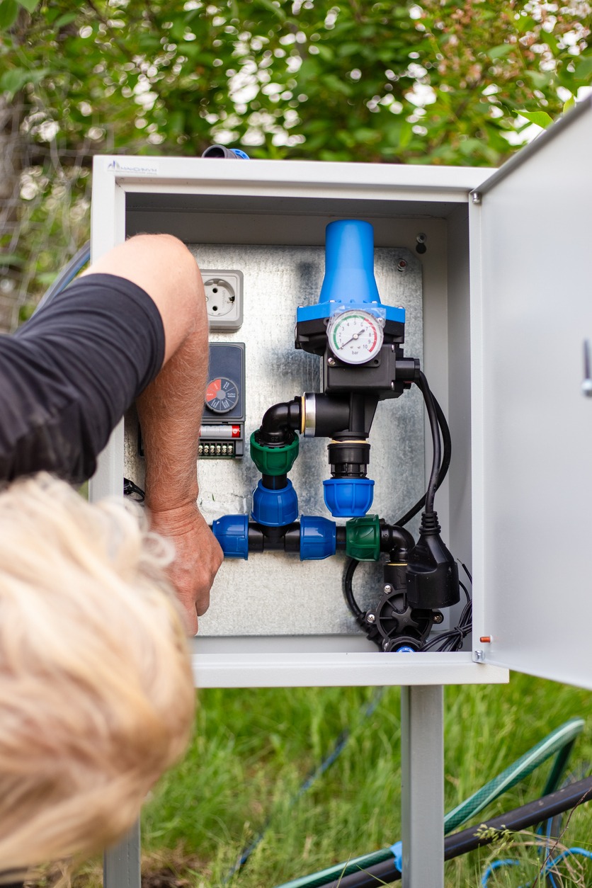 Person adjusts outdoor irrigation control box with pressure gauge